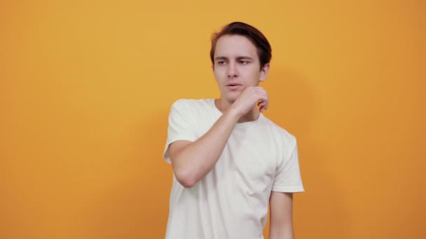 schöner junger Mann denkt, stützt sein Kinn mit der Hand in weißem T-Shirt - Filmmaterial, Video
