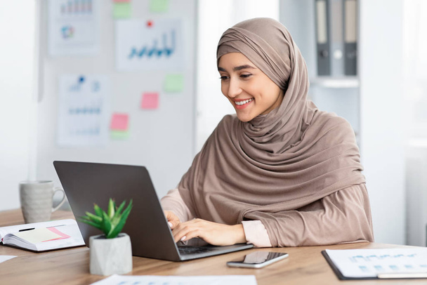 Boldog iszlám nő hidzsáb dolgozik laptop az irodában - Fotó, kép