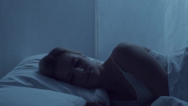 Young woman lying in the bed at night and having insomnia disease. Beautiful blond sleeping girl. Twilight in the bedroom, moonlight from the window. Sleeplessness, health and rest concept. - Filmmaterial, Video
