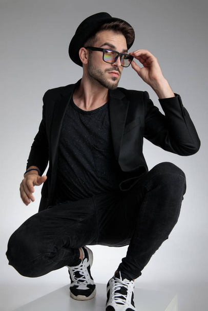 cool young man fixing glasses and crouching - Photo, image