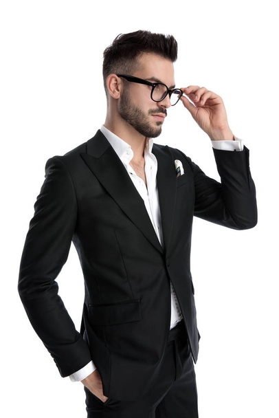 бизнесмен, стоящий с рукой в кармане и фиксирующий очки
 - Фото, изображение