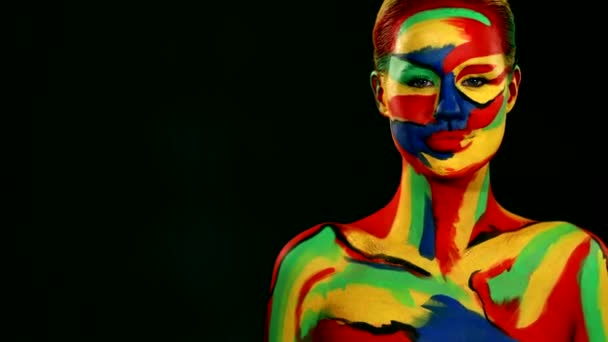 Γυναίκα με έγχρωμη ζωγραφική προσώπου και σώματος. Κορίτσι με φωτεινά πολύχρωμα μακιγιάζ και bodyart δείχνει προς τα δεξιά - Πλάνα, βίντεο