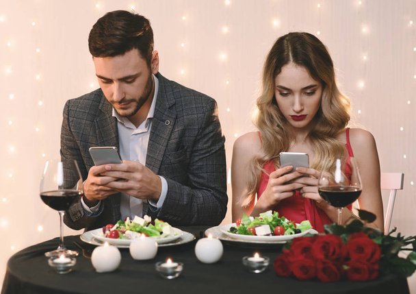 Ζευγάρι ξοδεύουν χρόνο με τα smartphones τους σε ρομαντική ημερομηνία στο εστιατόριο - Φωτογραφία, εικόνα