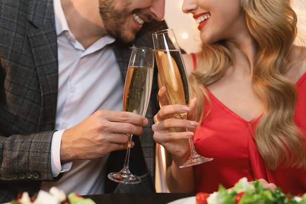 Champagne glasses in hands of unrecognizable couple at romantic dinner - Photo, Image