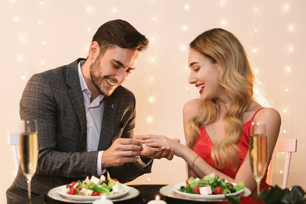 Hombre poniendo anillo de compromiso en novias mano en la fecha en el restaurante
 - Foto, imagen