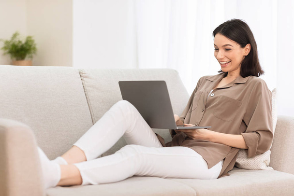 Молодая девушка работает на ноутбуке онлайн на диване
 - Фото, изображение
