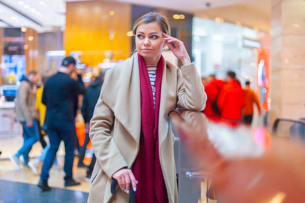 At the mall lifestyle fashion portrait of stunning brunette girl. Walking on At the mall. Going shopping. Wearing stylish white fitted coat, red neckscarf, black umbrella cane. Business woman. - Фото, зображення