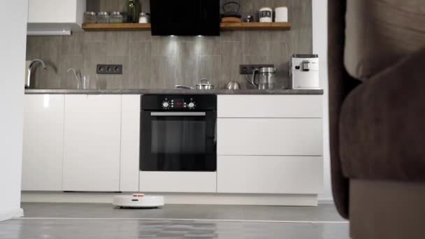 In a stylish modern kitchen is cleaning. The automatic robot vacuum cleaner moves along its trajectory. Elements of a smart home make life easier for people - Video, Çekim
