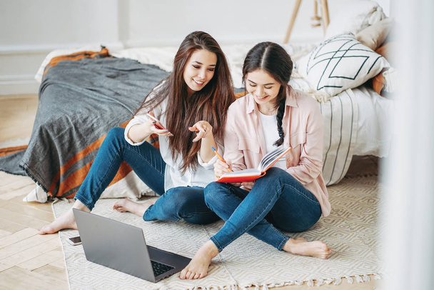 Giovani ragazze brune amiche studenti in casual fare progetto insieme alla ricerca di informazioni in internet da cellulare e laptop in camera
 - Foto, immagini