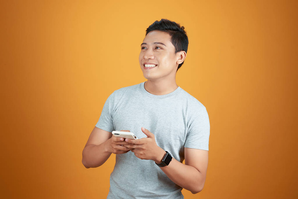 Smart casual asian man using smartphone in orange background. - Photo, Image