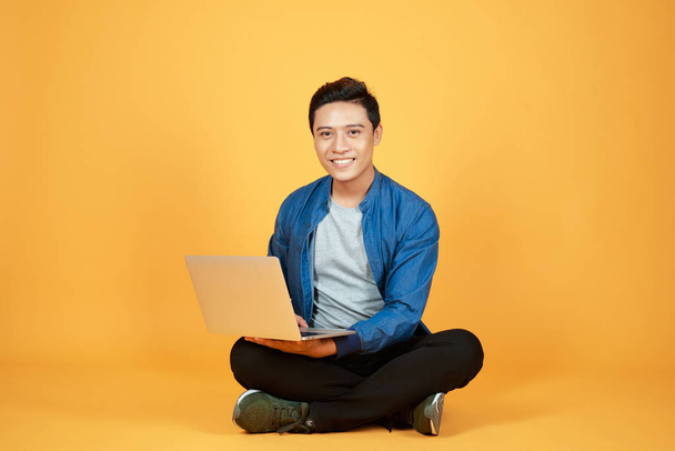 Asian man use of the laptop computer against color orange background - Foto, afbeelding