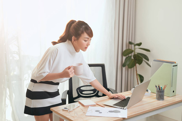 Прекрасна дівчина з Азії, яка використовує ноутбук, а в офісі тримає чай. - Фото, зображення