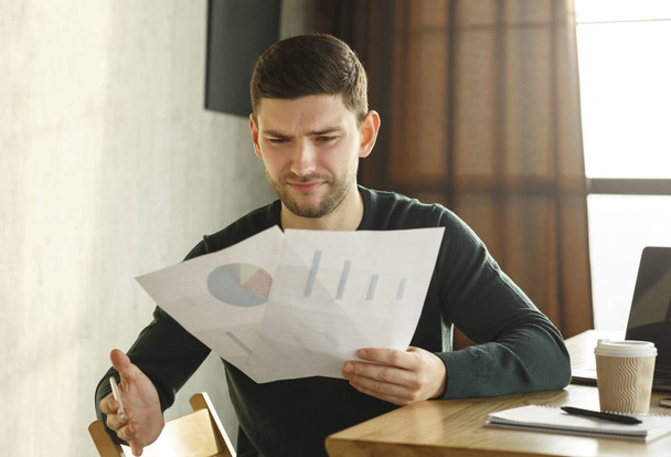 Discontented Office Worker Looking At Documents Sitting In Modern Office - Photo, Image