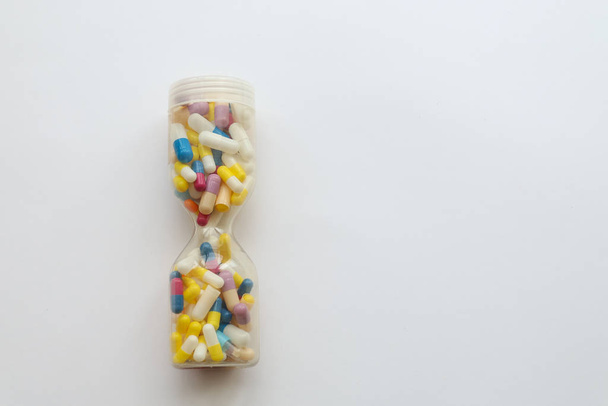 Hourglass with pills.  Meaninging of life. Medications  on white background. - Fotó, kép