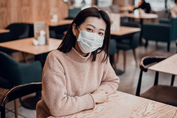 Mujer asiática en una máscara protectora está sentado en un café. Proteger a la población de los virus protegiendo el tracto respiratorio. El concepto de coronavirus en la vida cotidiana
 - Foto, imagen