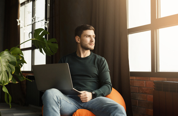 Millennial Guy pracuje na laptopie siedzi w fotelu Beanbag Indoor - Zdjęcie, obraz
