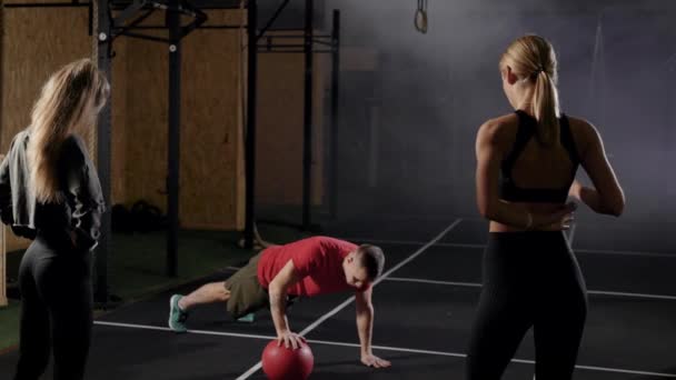 Trenéři v tělocvičně. Muž ukazuje cvičení dvěma mladým ženám. Blondýnky se naučí správnou techniku cvičení. - Záběry, video