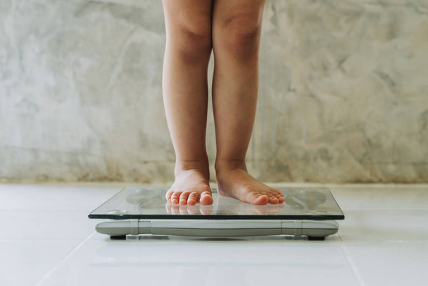 klein meisje op gewicht schaal op vloer achtergrond, Dieet concept. - Foto, afbeelding