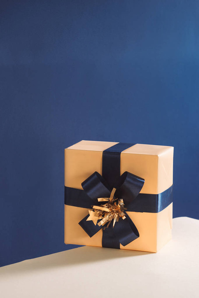 Wrapped gift box with blue ribbon bow, isolated on blue background - Photo, Image