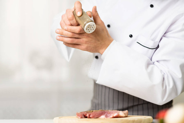 Onherkenbare mannelijke kok koken en kruiden vlees biefstuk in de keuken - Foto, afbeelding