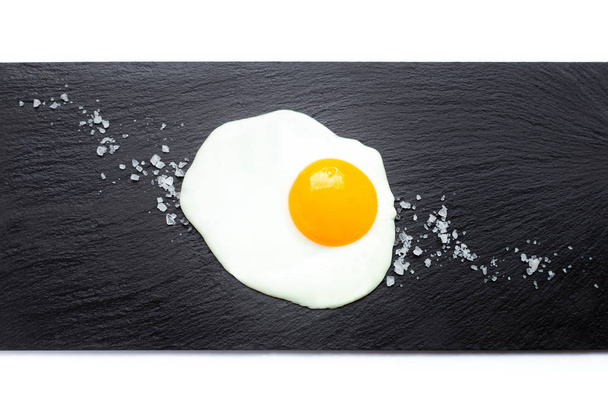 Gebakken ei op leisteen met zout op witte achtergrond. Koken en voedselconcept. - Foto, afbeelding