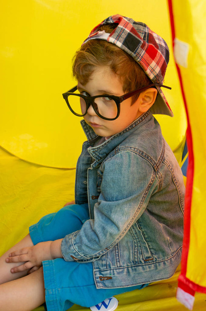 Child calm strict face on yellow background, outdoor. Kid strictly warning you. Kid boy with eyeglasses and cap, summer. - Zdjęcie, obraz