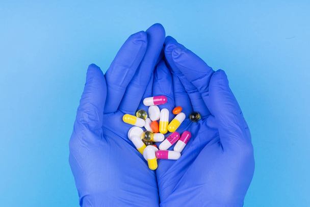 Different pills in hand in a medical glove on a blue background. Medicine. Treatment. - Foto, imagen