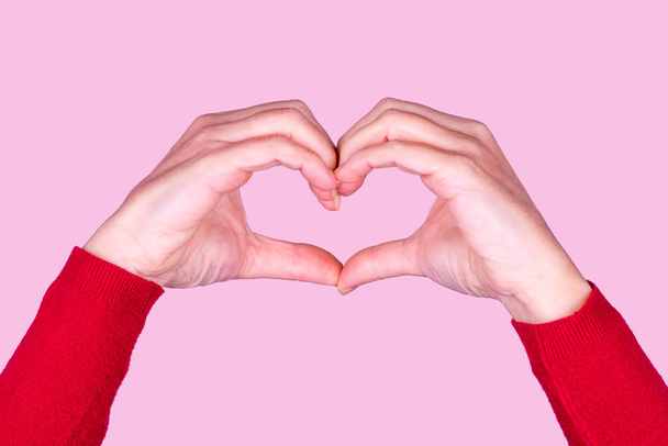 Female hands in the shape of a heart on a pink background. Valentines Day, Mothers Day background. - Fotografie, Obrázek