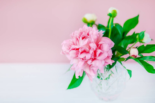 Pink peonies in a crystal vase on a pink wood background. - Fotó, kép