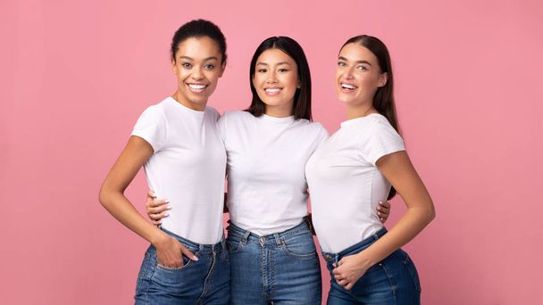 Tres mujeres abrazando de pie en el estudio sobre fondo rosa, Panorama
 - Foto, imagen