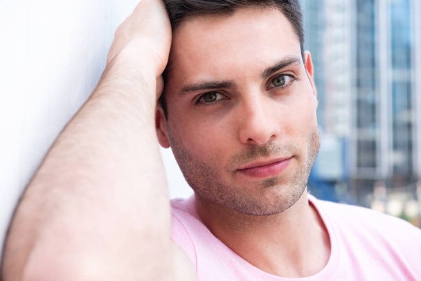 Close up portrait of handsome young man leaning against white wall - Photo, Image