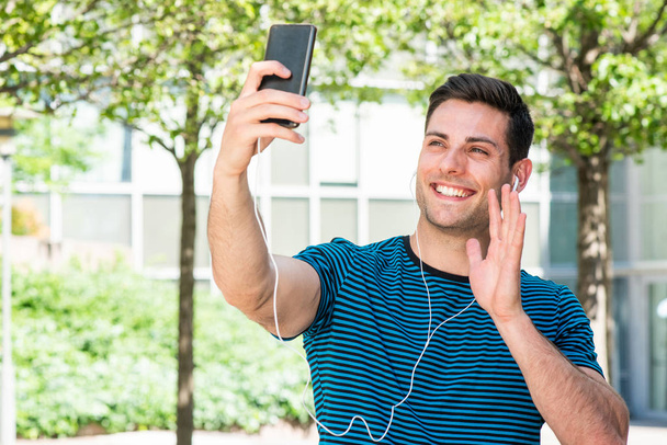 Retrato feliz joven sosteniendo el teléfono tomando selfie afuera en la ciudad
 - Foto, Imagen