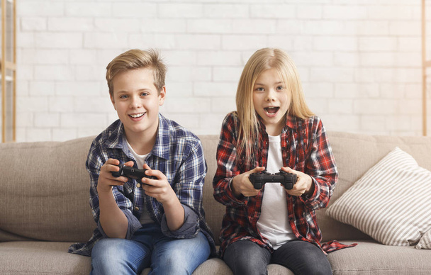 Schattige broer en zus spelen videospel zitten op de bank - Foto, afbeelding
