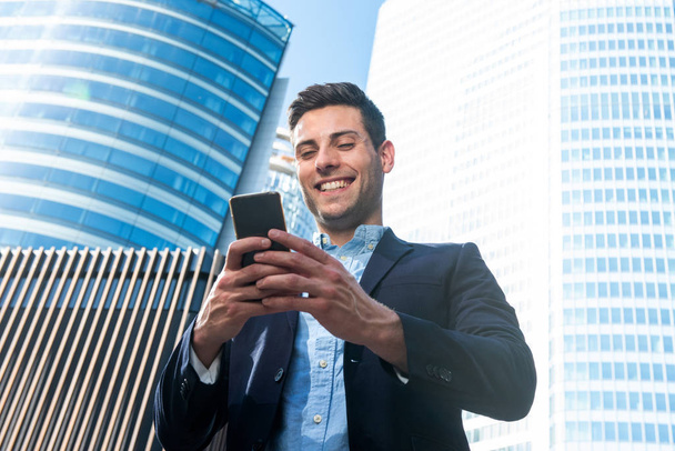 Portrait smiling business man standing in city looking at mobile phone  - Photo, image