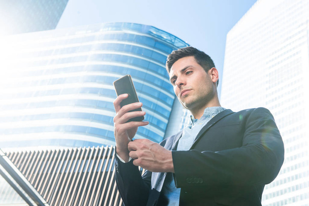 Portrait of young businessman looking at mobile phone in city - Photo, image