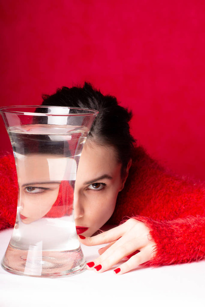 beautiful young girl in red, red background, a vase of water, reflection - Photo, Image