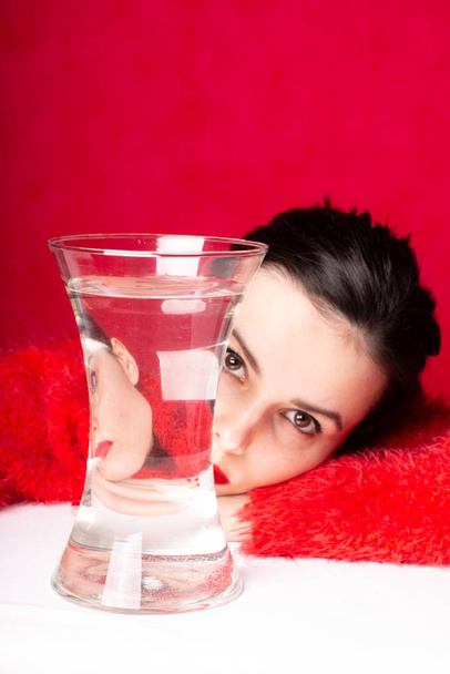 beautiful young girl in red, red background, a vase of water, reflection - Foto, Bild