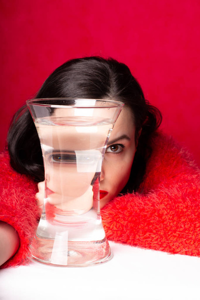 beautiful young girl in red, red background, a vase of water, reflection - Фото, изображение