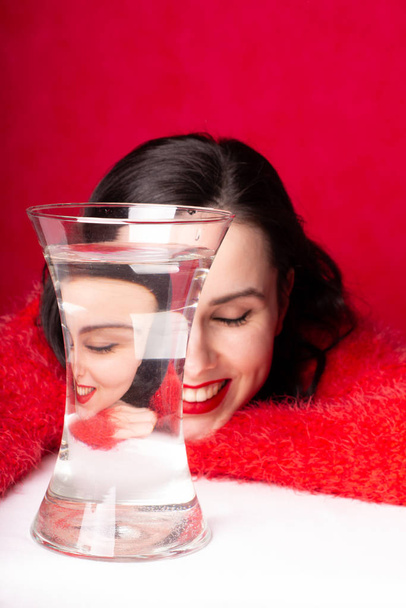 beautiful young girl in red, red background, a vase of water, reflection - Fotografie, Obrázek