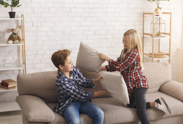 Happy Brother And Sister Having Pillow Fight On Couch Indoor - Foto, Imagem