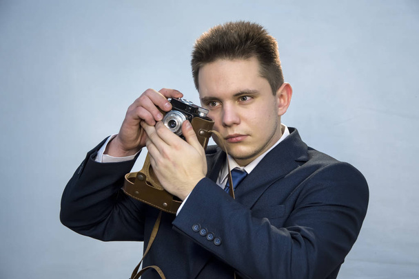 Portrait of a young man in a suit with an old camera, perhaps he is a novice journalist doing a report, a diplomat or secret agent photographing documents, a businessman collecting dirt - Photo, Image