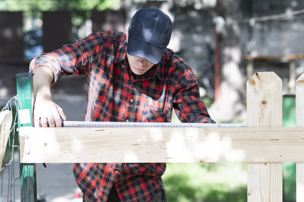 Νεαρός ξυλουργός που μετρά το ξύλο χρησιμοποιώντας ένα μέτρο ταινία στο gard - Φωτογραφία, εικόνα