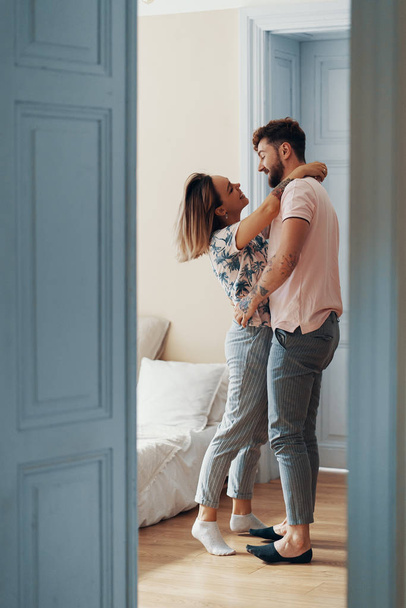 Вид профілю люблячої молодої пари, що обіймається, стоячи у своїй спальні
 - Фото, зображення