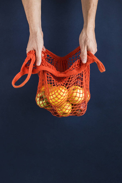 Maçãs e limões em um saco de corda laranja nas mãos dos homens em um da
 - Foto, Imagem