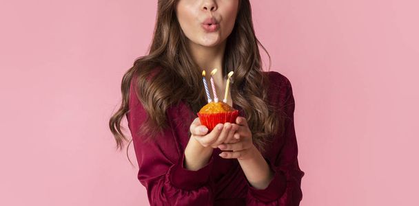 Donna irriconoscibile che soffia candele colorate sul cupcake di compleanno
 - Foto, immagini