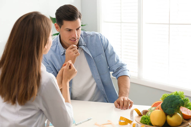 Young nutritionist consulting patient at table in clinic - Photo, Image