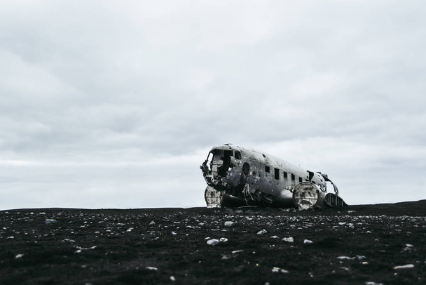 The remains of the wrecked plane on the black sand beach in Iceland under the heavy grey clouds. - Zdjęcie, obraz