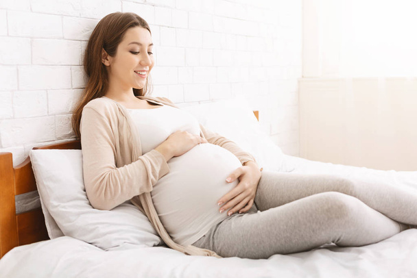Przyszła matka ciesząca się ciążą, dotykając swojego wielkiego brzucha - Zdjęcie, obraz