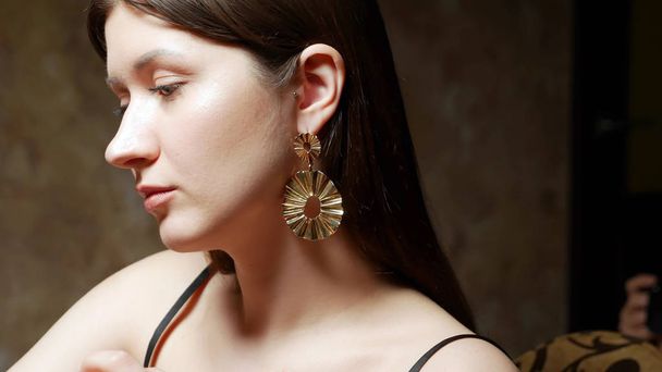 young beautiful stylish girl wears earrings. the dark background - Fotografie, Obrázek