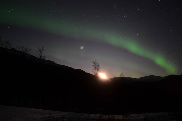 Aurora borealis pierce the night sky and the moon is rising up behind the mountain - Foto, Bild